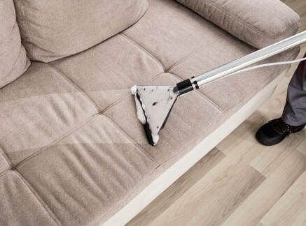 Couch upholstery being cleaned professionally in a residence with commercial steam cleaning equipment.